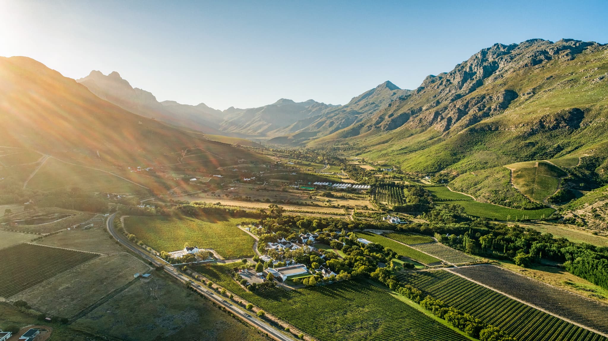 Aerial view of Stellenbosch valley at golden hour with vineyards, farms, and Helderberg mountains