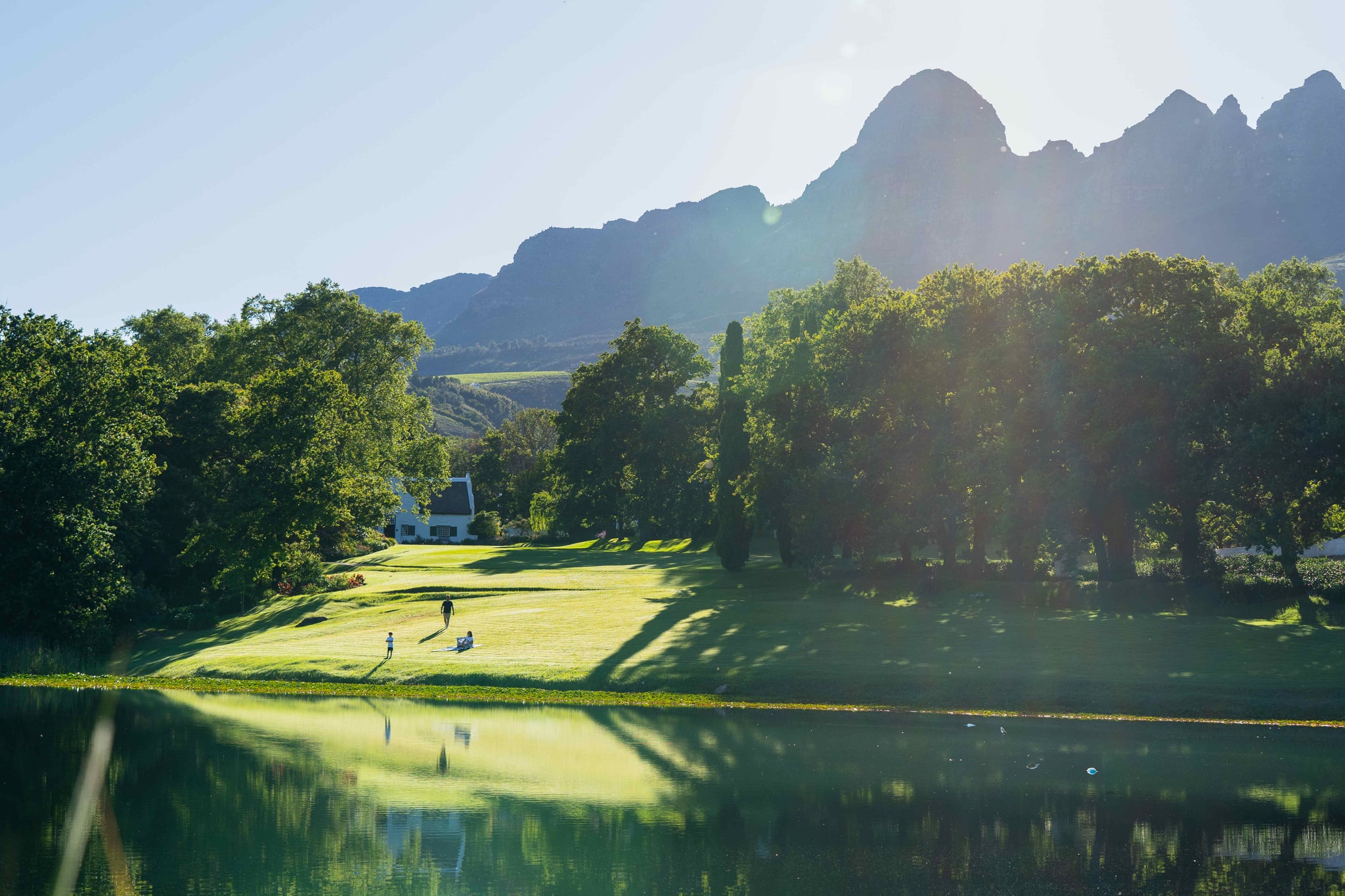 Lake with Helderberg mountains, manor house on green lawn at golden hour