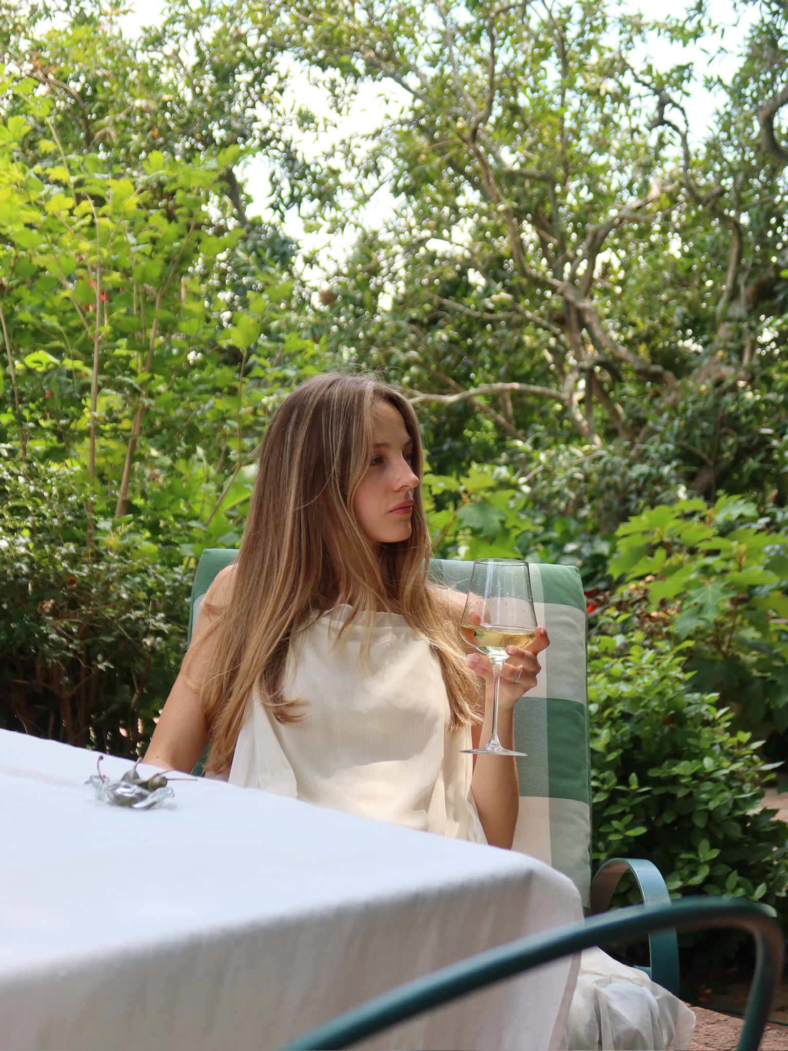 Woman enjoying a glass of white wine at an outdoor garden table